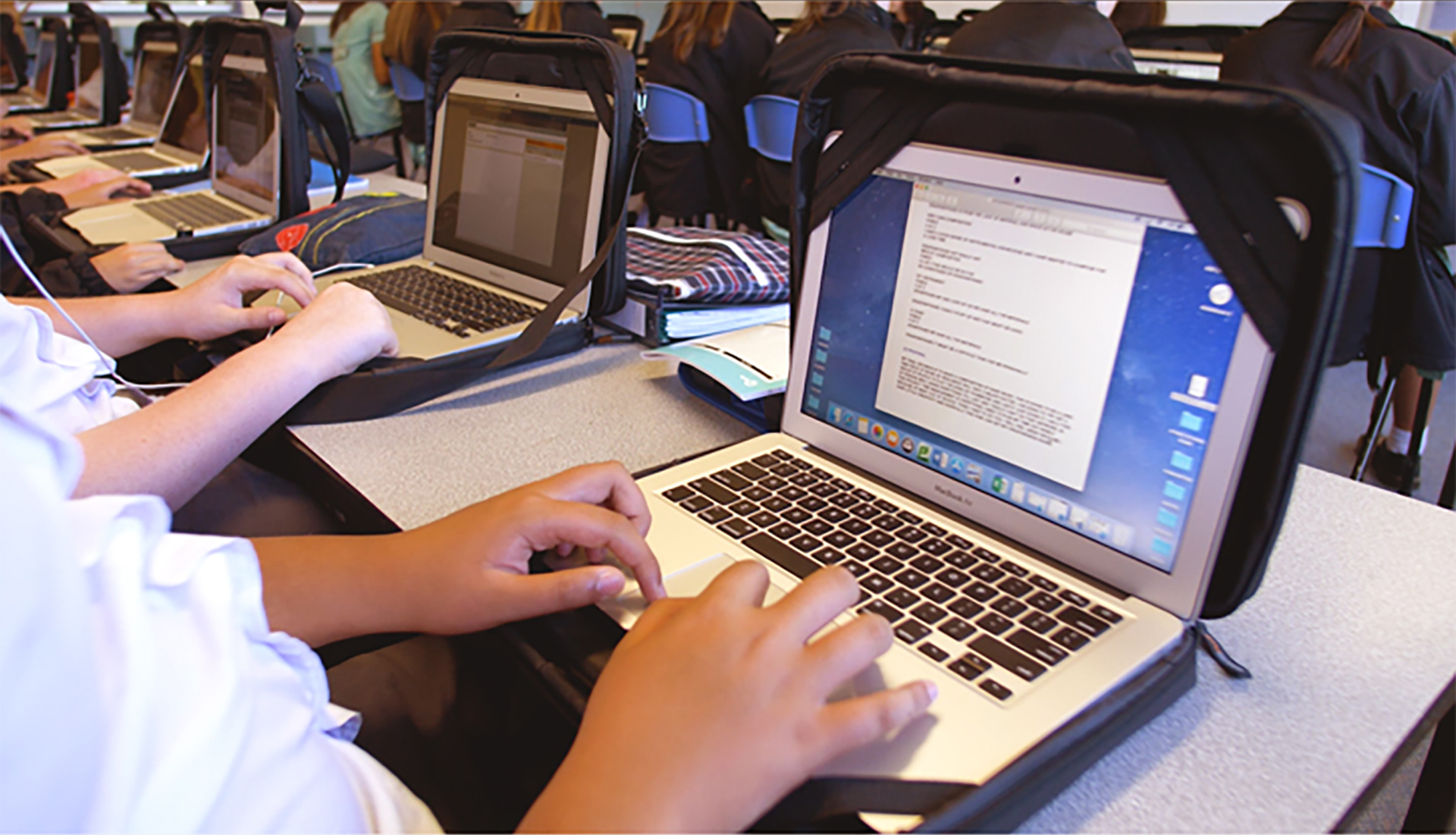 A row of children with open laptops in protective bags